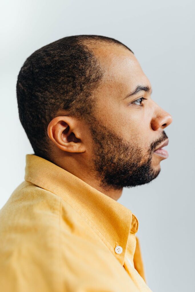 Side profile of a man wearing a yellow shirt, captured indoors.